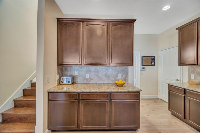 kitchen with light stone counters, light wood-style floors, decorative backsplash, baseboards, and dark brown cabinets