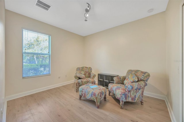 living area with track lighting, wood finished floors, visible vents, and baseboards