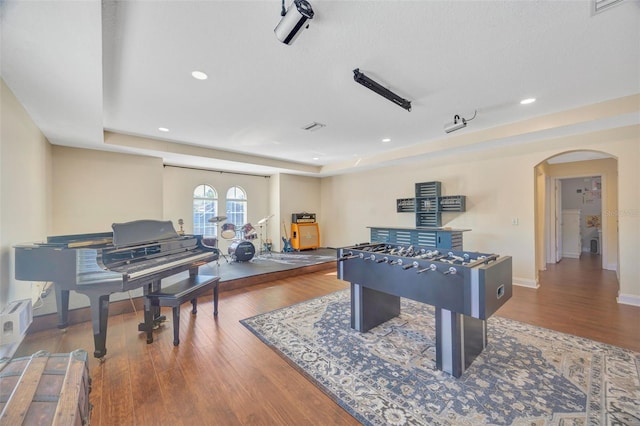 game room featuring baseboards, a tray ceiling, recessed lighting, wood finished floors, and arched walkways