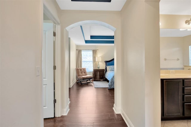 hallway featuring wood finished floors, arched walkways, and baseboards