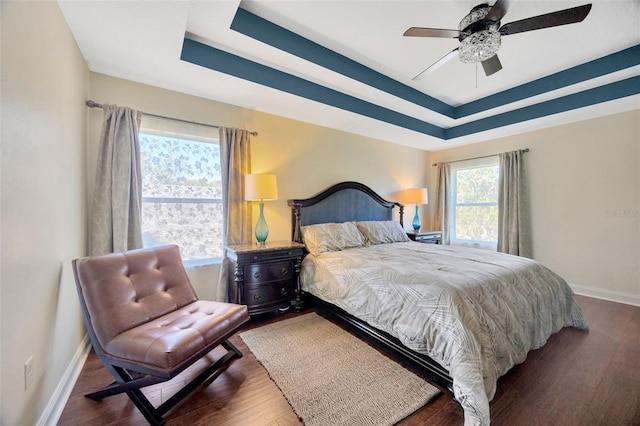 bedroom featuring ceiling fan, baseboards, a raised ceiling, and wood finished floors