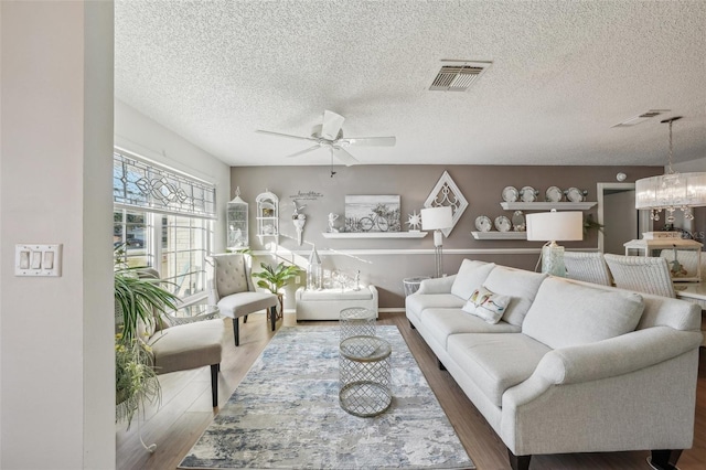 living room with baseboards, visible vents, a ceiling fan, wood finished floors, and a textured ceiling