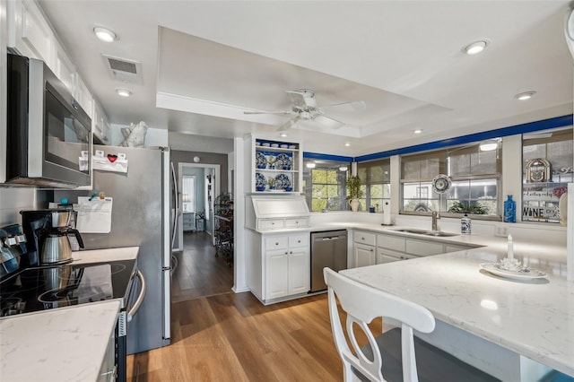 kitchen with light stone counters, light wood-style flooring, stainless steel appliances, visible vents, and a tray ceiling