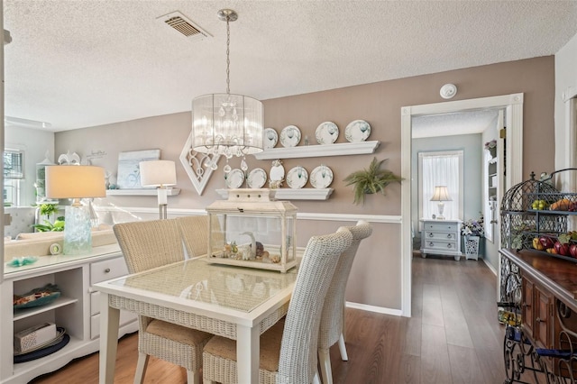 dining space with a textured ceiling, visible vents, a chandelier, and wood finished floors