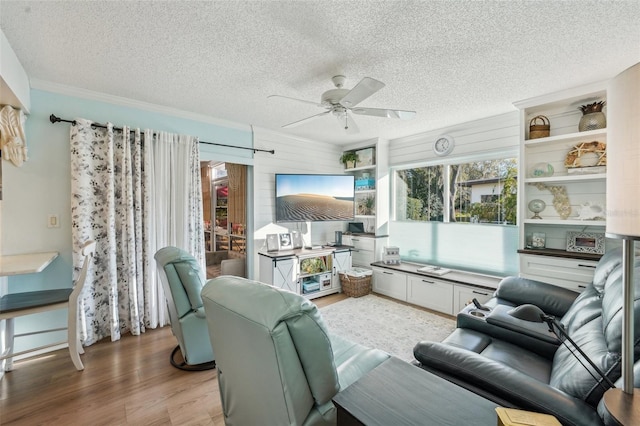 living room with ceiling fan, a textured ceiling, light wood-style flooring, and crown molding