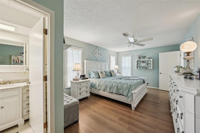 bedroom featuring visible vents, a ceiling fan, a sink, a textured ceiling, and wood finished floors