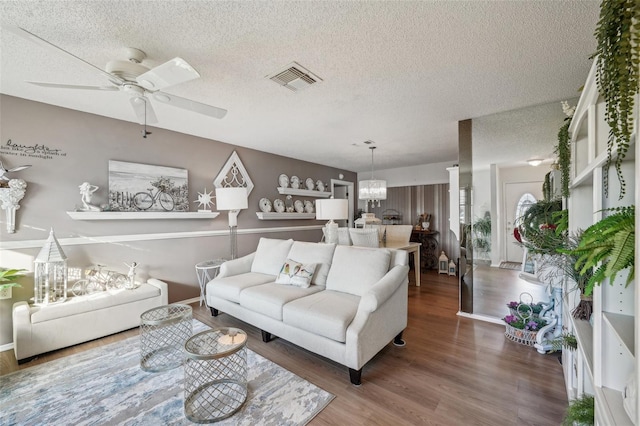 living area featuring a textured ceiling, visible vents, wood finished floors, and ceiling fan with notable chandelier