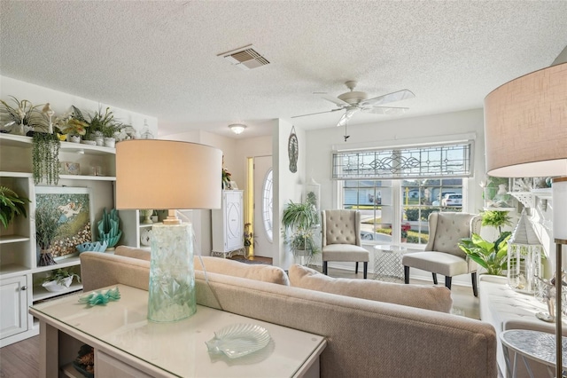 living room featuring a textured ceiling, dark wood-type flooring, visible vents, and a ceiling fan