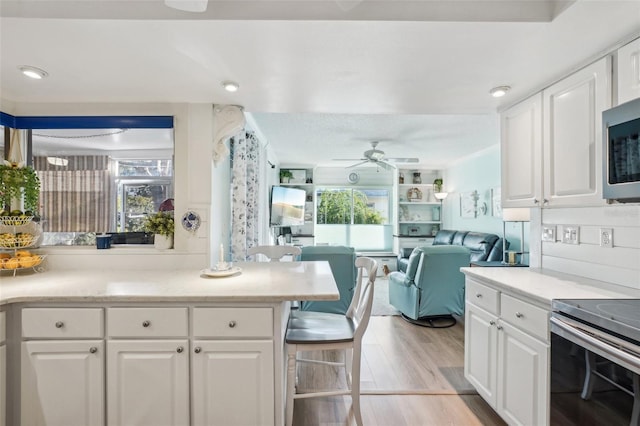 kitchen featuring light wood-style floors, open floor plan, white cabinetry, and appliances with stainless steel finishes