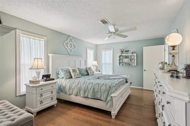 bedroom featuring dark wood-style flooring, visible vents, ceiling fan, a textured ceiling, and baseboards