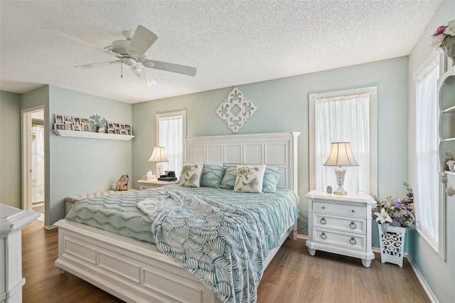 bedroom featuring ceiling fan, a textured ceiling, baseboards, and wood finished floors