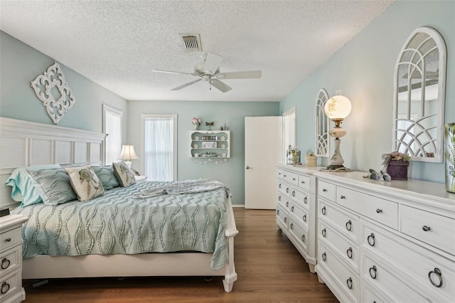 bedroom with dark wood-type flooring, visible vents, ceiling fan, and a textured ceiling