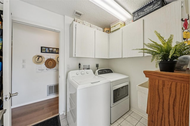 laundry room with cabinet space, light tile patterned flooring, visible vents, and washing machine and clothes dryer