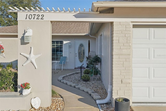 property entrance featuring a garage, roof with shingles, and stucco siding