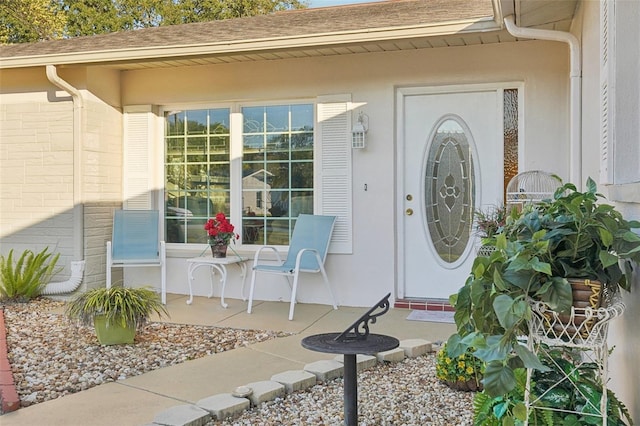 view of exterior entry featuring a shingled roof and stucco siding