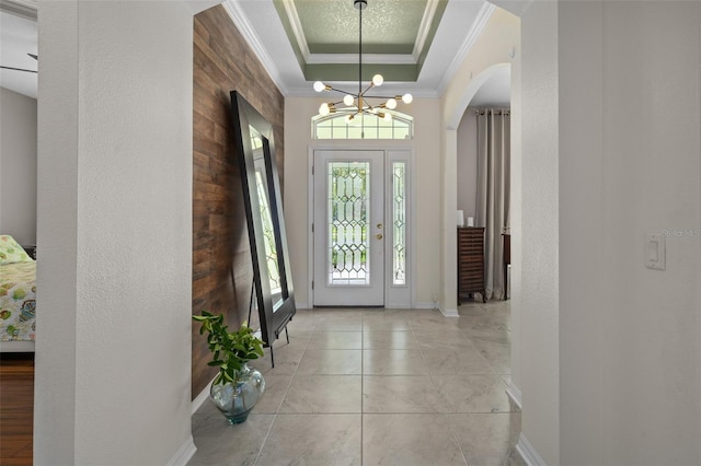 foyer with arched walkways, a textured wall, light tile patterned floors, a tray ceiling, and crown molding