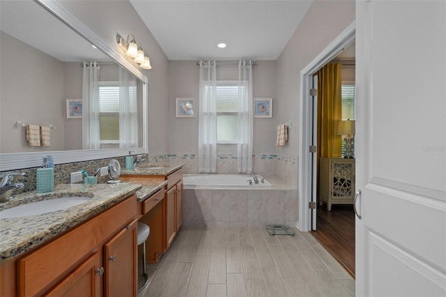 bathroom featuring a garden tub, double vanity, wood finished floors, and a sink