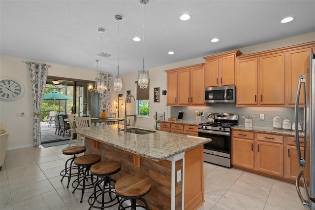 kitchen with light stone counters, stainless steel appliances, a sink, tasteful backsplash, and a kitchen bar