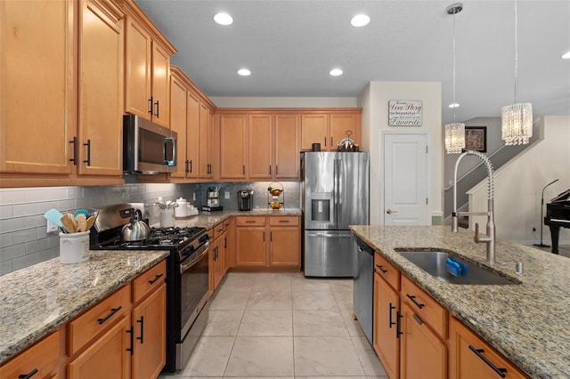 kitchen with decorative backsplash, appliances with stainless steel finishes, light stone countertops, pendant lighting, and a sink