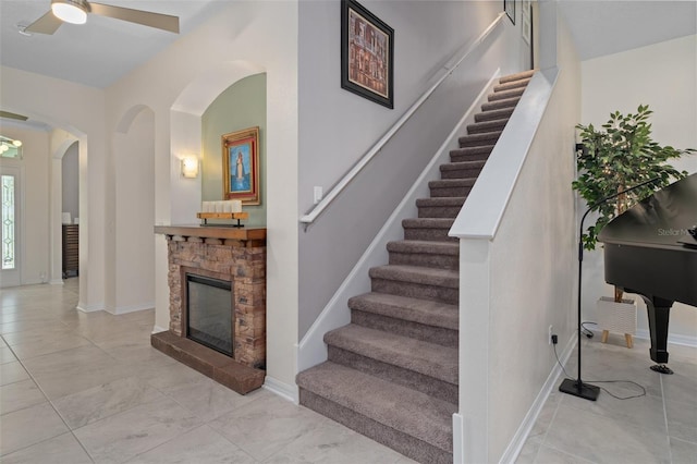 staircase featuring arched walkways, a fireplace, and baseboards