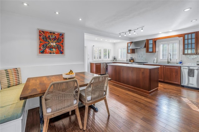 kitchen featuring appliances with stainless steel finishes, dark wood-style flooring, light countertops, wall chimney range hood, and backsplash