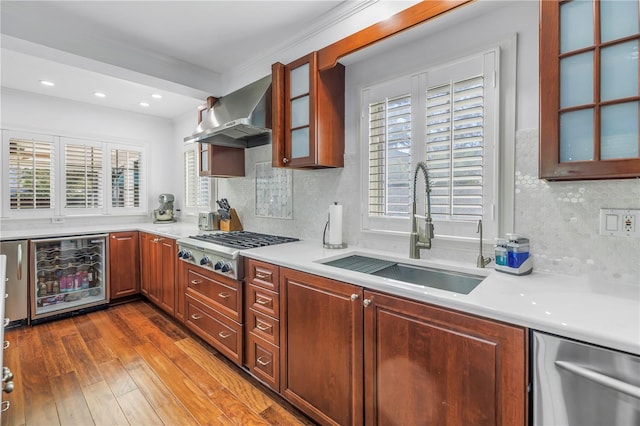 kitchen with wine cooler, light countertops, appliances with stainless steel finishes, a sink, and wall chimney range hood