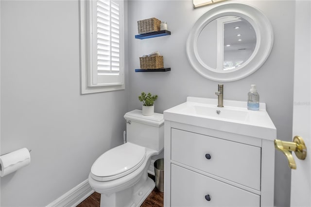 half bathroom featuring baseboards, vanity, toilet, and wood finished floors