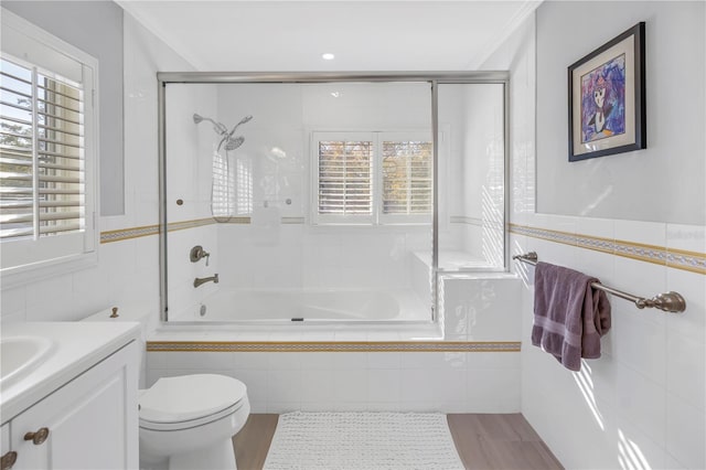 bathroom with toilet, wood finished floors, vanity, tile walls, and tiled shower / bath