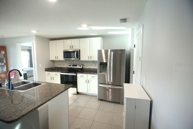 kitchen with light tile patterned floors, appliances with stainless steel finishes, a sink, white cabinetry, and backsplash