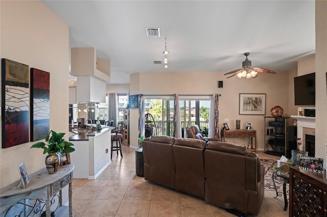 living room featuring light tile patterned floors, ceiling fan, a fireplace, and visible vents