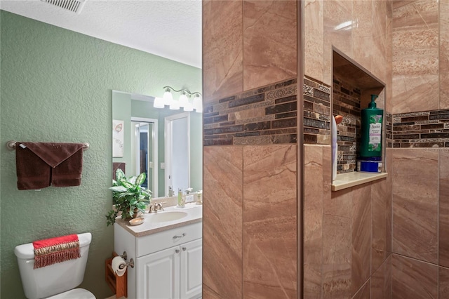 bathroom with visible vents, a textured wall, vanity, and toilet