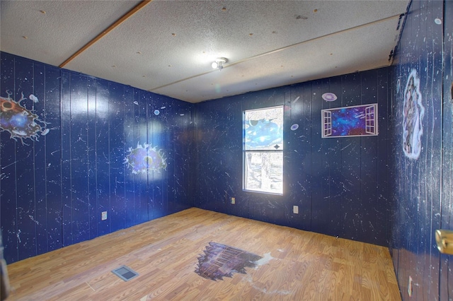 empty room with a textured ceiling, visible vents, and wood finished floors