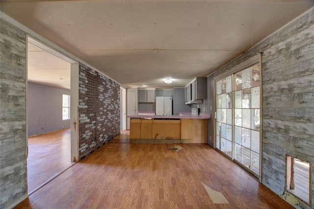 kitchen with wooden walls, tile countertops, freestanding refrigerator, a peninsula, and light wood-type flooring