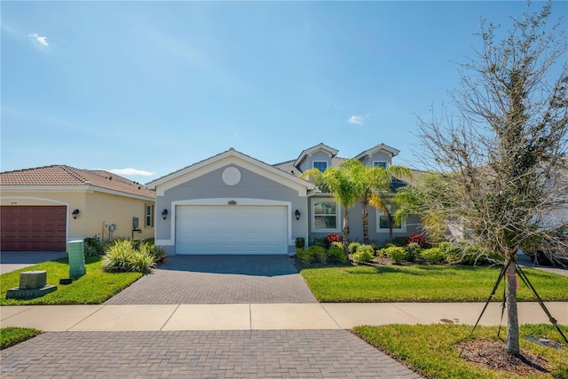 view of front of home with a garage, a front yard, decorative driveway, and stucco siding