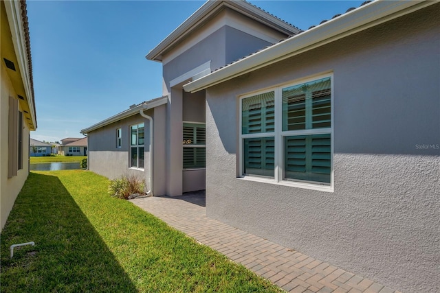 view of side of home with a water view, a lawn, and stucco siding