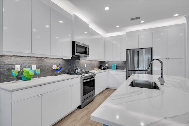 kitchen with visible vents, backsplash, appliances with stainless steel finishes, a sink, and modern cabinets