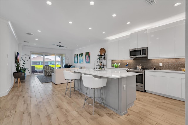 kitchen featuring a breakfast bar area, appliances with stainless steel finishes, backsplash, an island with sink, and modern cabinets