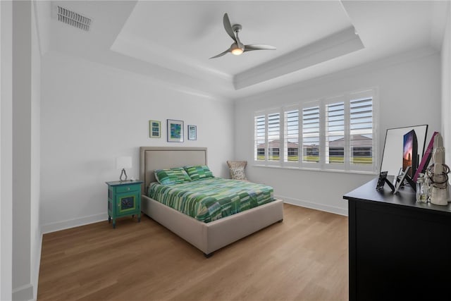 bedroom with a tray ceiling, visible vents, baseboards, and wood finished floors