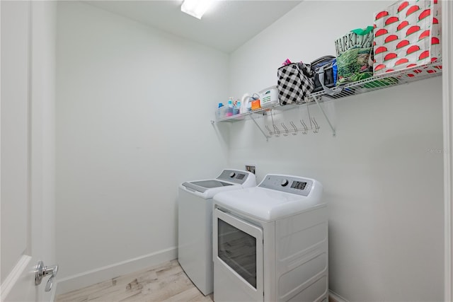 clothes washing area featuring laundry area, baseboards, light wood finished floors, and washing machine and clothes dryer