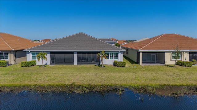 rear view of property featuring a lawn, a sunroom, a tiled roof, a water view, and stucco siding