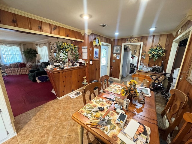 dining area featuring ornamental molding, visible vents, wooden walls, and light tile patterned flooring