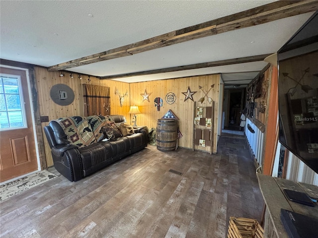 living room featuring a textured ceiling, beamed ceiling, wood finished floors, and wooden walls