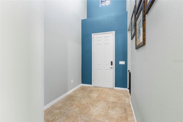 foyer entrance with light tile patterned floors, a high ceiling, and baseboards