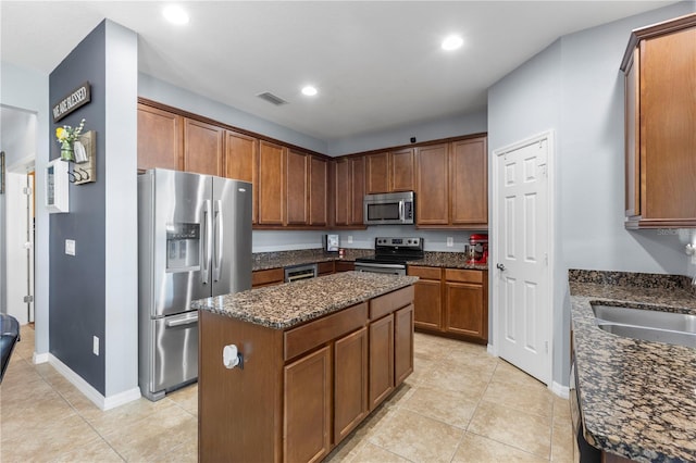 kitchen featuring stainless steel appliances, visible vents, a kitchen island, a sink, and dark stone counters