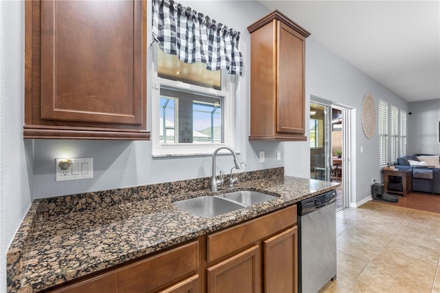 kitchen with light tile patterned floors, dark stone counters, open floor plan, stainless steel dishwasher, and a sink