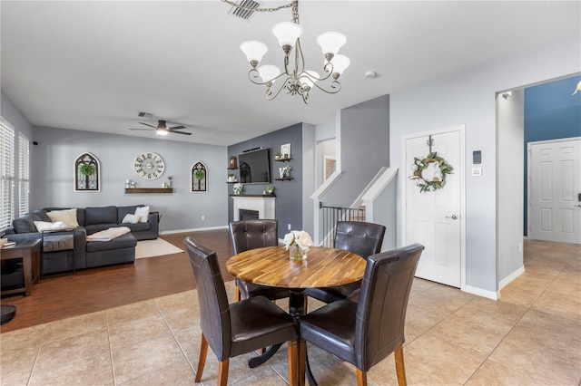 dining room featuring a fireplace, light tile patterned floors, visible vents, baseboards, and ceiling fan with notable chandelier