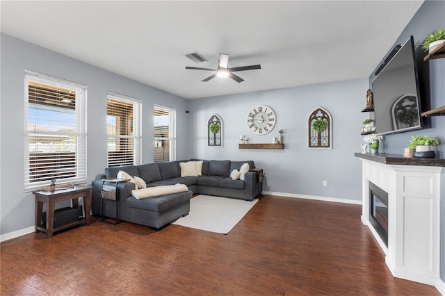 living area with visible vents, dark wood-type flooring, a glass covered fireplace, a ceiling fan, and baseboards