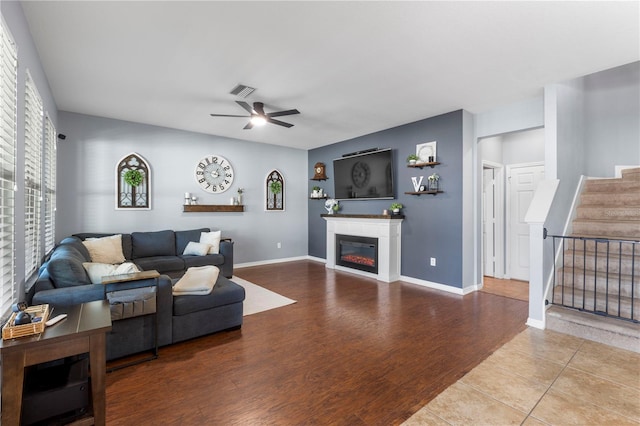 living area with baseboards, a ceiling fan, a glass covered fireplace, wood finished floors, and stairs