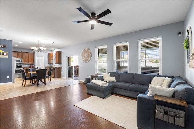 living room with ceiling fan with notable chandelier, recessed lighting, baseboards, and light wood-style floors