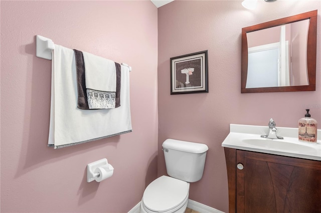 half bath featuring baseboards, vanity, and toilet